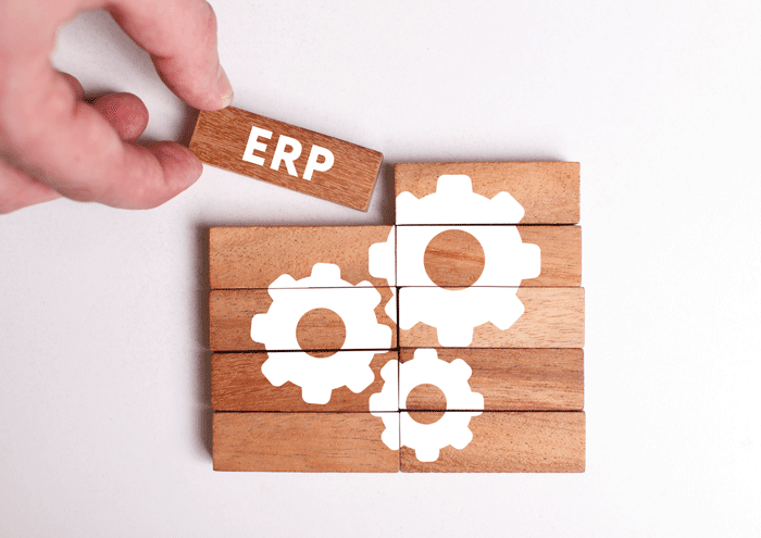Main posant un bloc de bois marqué ERP sur un assemblage de blocs illustré d'engrenages, symbole d'un logiciel de gestion intégré