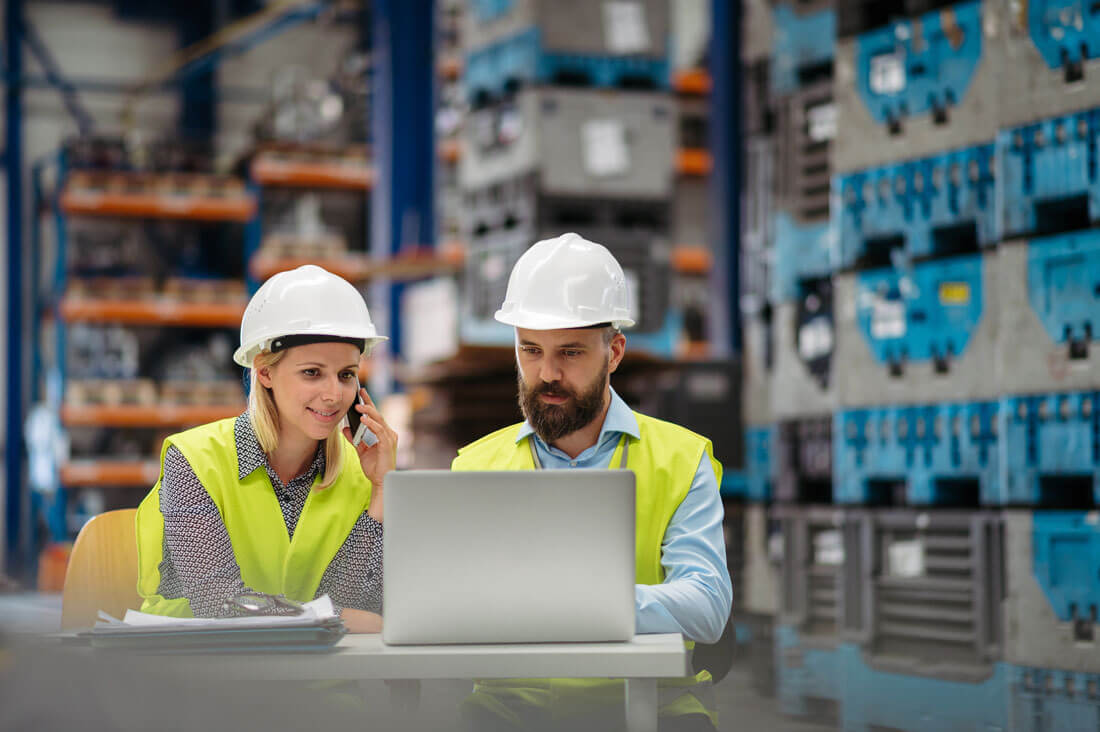 Deux ingénieurs analysant des données de production sur un ordinateur portable dans un entrepôt industriel