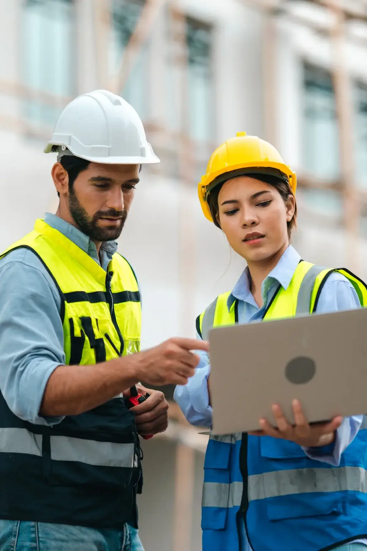 Deux responsables de chantier en casque consultant un suivi de projet sur ordinateur portable